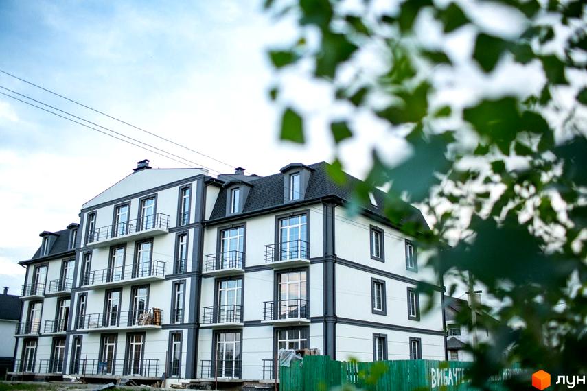 Клубний будинок Giverny HOUSE з біло-сірим фасадом та балконами. Навколо зелені дерева та паркан.