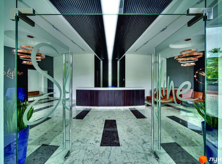 Житловий комплекс Skyline: сучасний вхід з двома скляними дверима, рецепцією та м'якими меблями в зоні очікування.