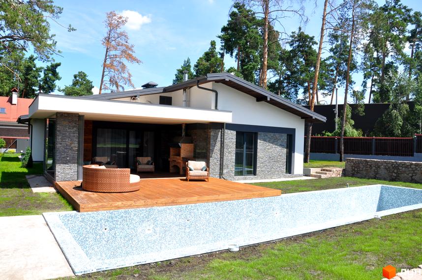 Будинок з панорамними вікнами та терасою з дерев'яним настилом. На території розташований басейн та зелена галявина. Котеджне містечко Хвойний квартал.