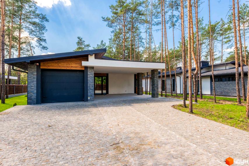 Будинок Котеджного містечка Хвойний квартал з темним гаражем, кам'яним облицюванням та білими стінами. Навколо високі сосни та брукована доріжка.