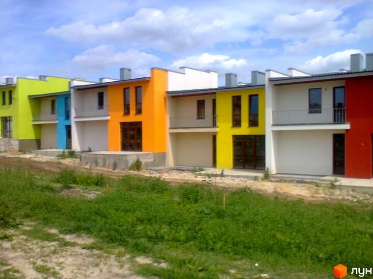 Яскраві таунхауси «Фільварок» з кольоровими фасадами. Зелена прибудинкова територія з травою та кущами.