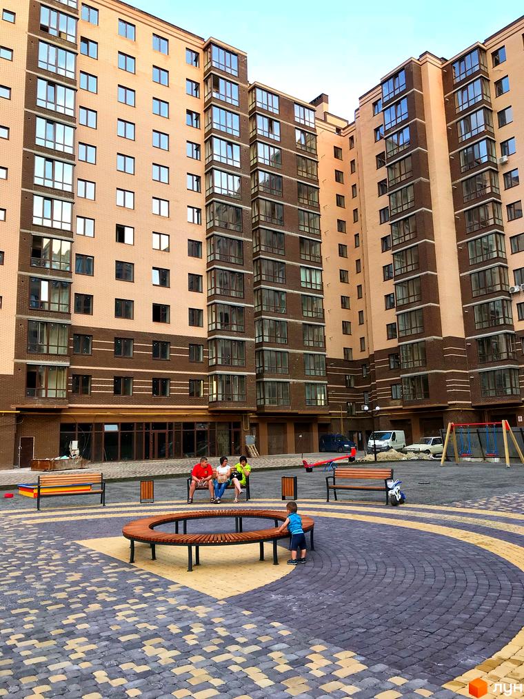 Зовнішній вигляд багатоповерхових будинків ЖК Андорра з цегляним фасадом та великими вікнами. Прибудинкова територія з дитячим майданчиком та місцями для відпочинку.