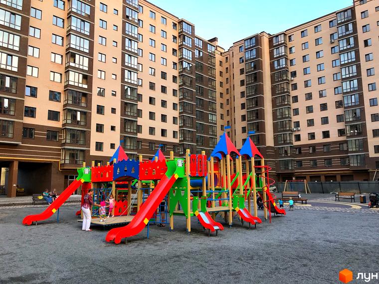 Житловий комплекс Андорра: фасади будинків з цегляним оздобленням та дитячий майданчик з гірками та гойдалками.