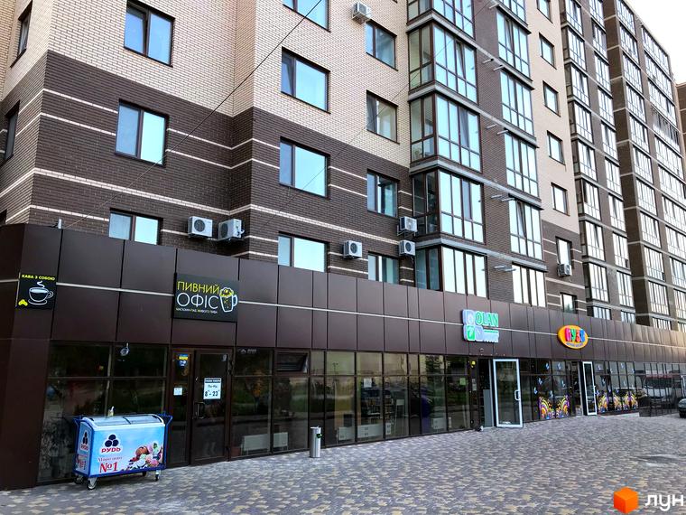 Зображення фасаду Житлового комплексу Андорра з магазинами на першому поверсі. Багатоповерхова будівля з вікнами та кондиціонерами.