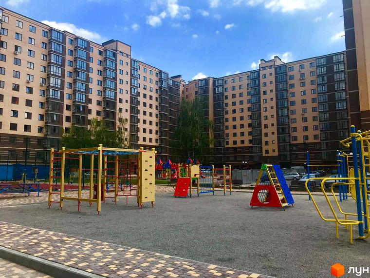 Житловий комплекс Андорра: багатоповерхові будинки з коричневою та бежевою обробкою фасаду. Поруч дитячий майданчик з різнокольоровими гірками та спортивними елементами.