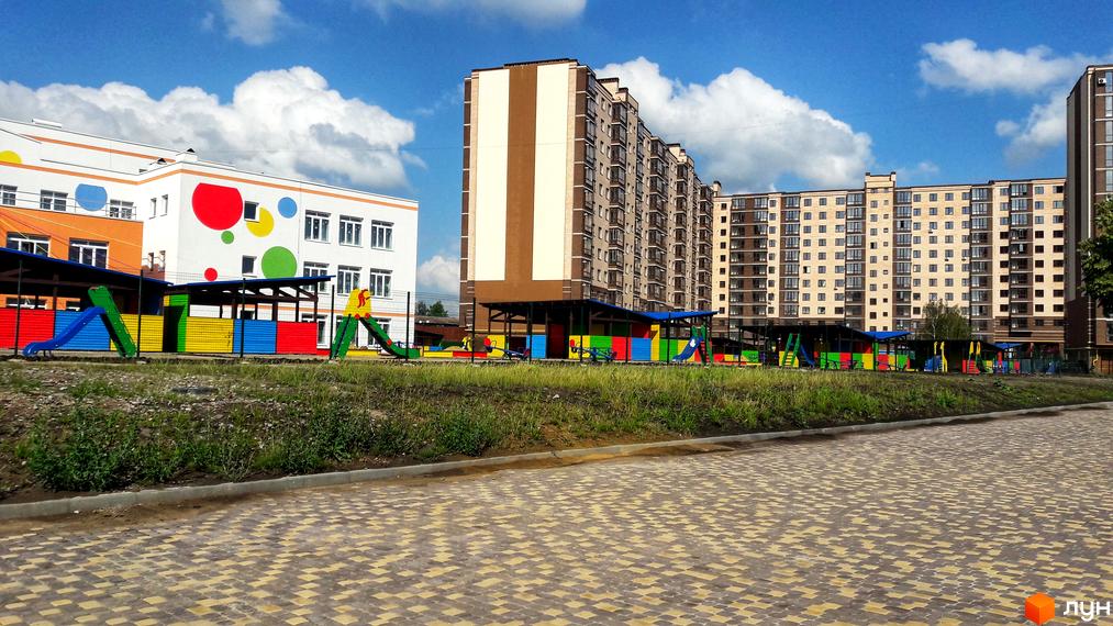 Житловий комплекс Андорра: фасади багатоповерхових будинків та дитячий майданчик з гірками та гойдалками. Територія комплексу з бруківкою та зеленими насадженнями.