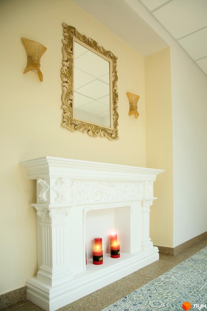 Елегантний білий камін з дзеркалом у золотій рамі та свічками, що створює затишну атмосферу в інтер'єрі ЖК Comfort Club. Стильний дизайн та вишукані деталі.
