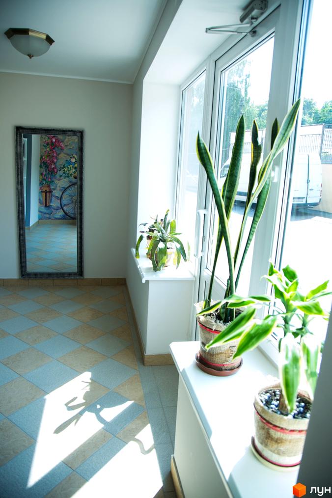 Інтер'єр житлового комплексу Comfort Club з дзеркалом та рослинами біля вікна. Сонячні промені падають на підлогу з плитки.