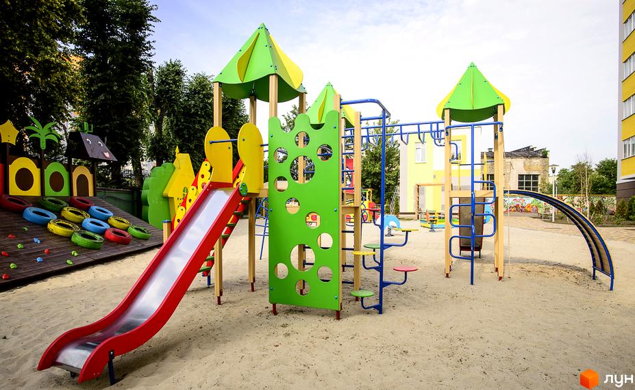 Дитячий майданчик з гіркою, гойдалками та елементами для лазіння на території житлового комплексу Відрадний. Безпечне покриття з піску та дерев'яні конструкції.