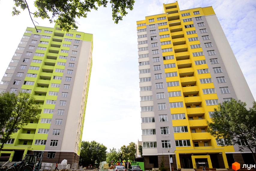 Житловий комплекс Відрадний: яскраві новобудови з зеленими та жовтими фасадами. Навколо новобудов зелені дерева та будівельні роботи.