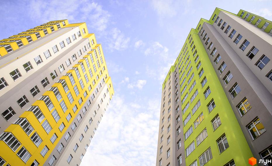 Житловий комплекс Відрадний - двоколірні багатоповерхові будинки з численними вікнами на тлі блакитного неба з хмарами. Зовнішній вигляд новобудов.