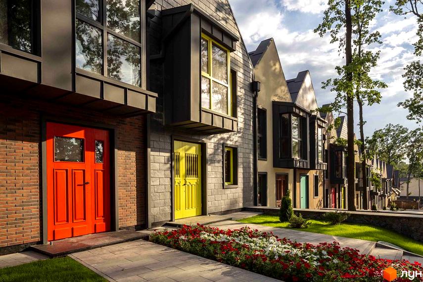 Котеджне містечко Oak Grove Town. Фасади будинків з цегли та сірої плитки, кольорові двері. Перед будинками газон, доріжки та клумби з квітами.