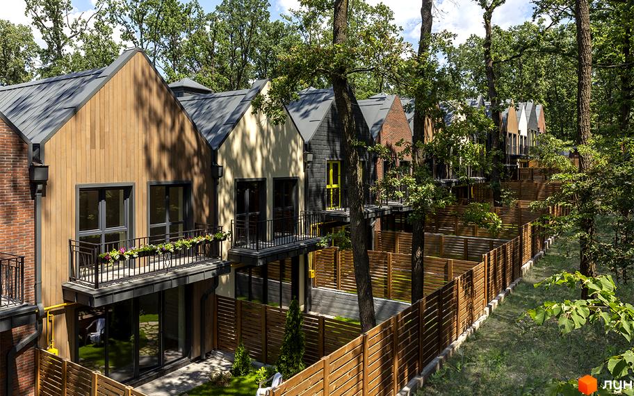 Ряд котеджів Котеджного містечка Oak Grove Town з різними фасадами та темними дахами. Будинки оточені високими деревами та дерев'яними огорожами.