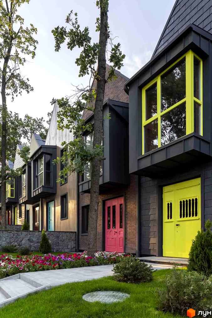 Котеджне містечко Oak Grove Town: фасади будинків темні з яскравими вікнами та дверима. Прибудинкова територія: зелений газон та квіткові клумби.