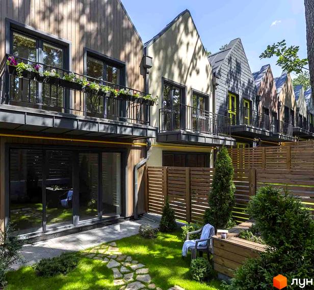 Котеджне містечко Oak Grove Town: ряд будинків з різними фасадами, балконами та зеленими газонами. На подвір'ї доріжка з каменів та дерев'яні огорожі.