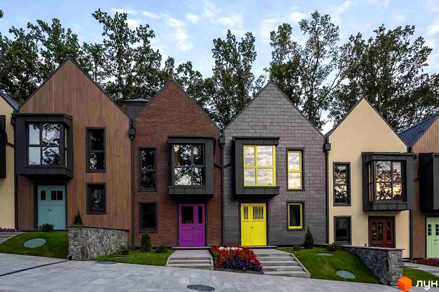 Зображення фасаду будинку КМ Oak Grove Town. Будинки з різними кольорами дверей та оздобленням фасадів. Перед будинками газон та доріжки з бруківки.