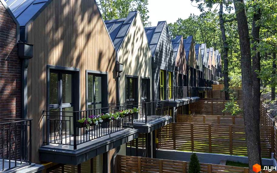 Ряд котеджів Котеджного містечка Oak Grove Town з фасадами з дерева, штукатурки та цегли, балконами. Прибудинкова територія оточена лісом та дерев'яними огорожами.