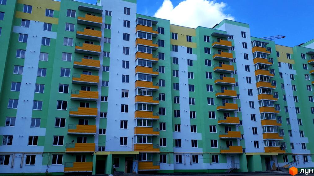 Зовнішній вигляд багатоповерхового будинку в Житловому комплексі Райдужний з яскравими балконами. Фасад будинку пофарбовано в зелений та білий кольори, блакитне небо.