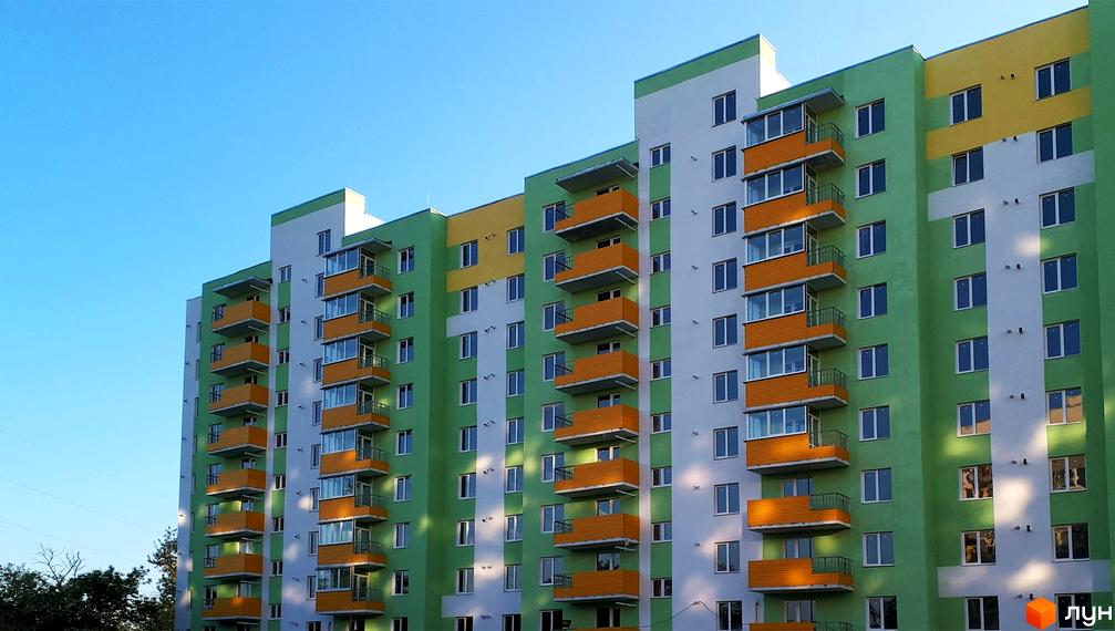 Зовнішній вигляд багатоповерхового будинку в Житловому комплексі Райдужний. Фасад будинку пофарбований у зелений, жовтий та білий кольори, є балкони.