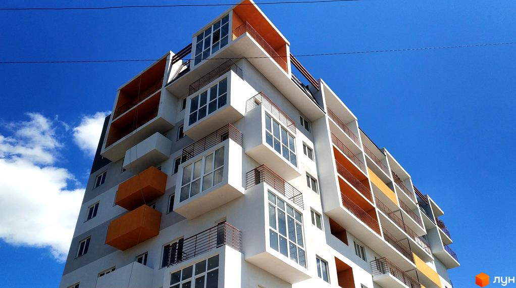 Житловий комплекс Gaudi Hall з яскравими оранжевими елементами та скляними балконами на фоні блакитного неба. Сучасна архітектура новобудови.