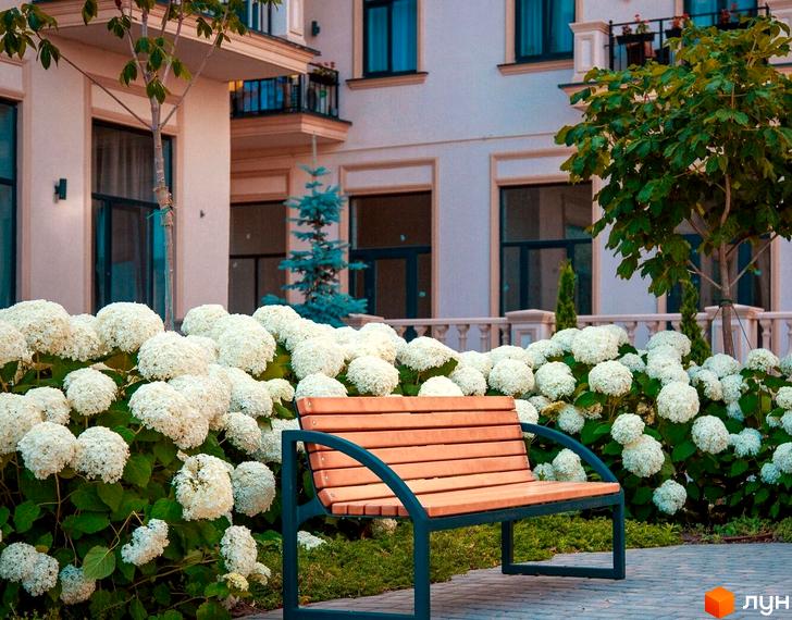 Фасад будинку Житлового кварталу Авторський з великими вікнами та балконами, на передньому плані лавка серед білих гортензій та зелених насаджень.