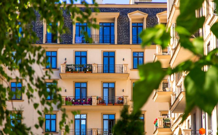 Фасад багатоквартирного будинку Житлового кварталу Авторський з мансардним дахом, балконами з квітами та зеленими деревами на передньому плані.