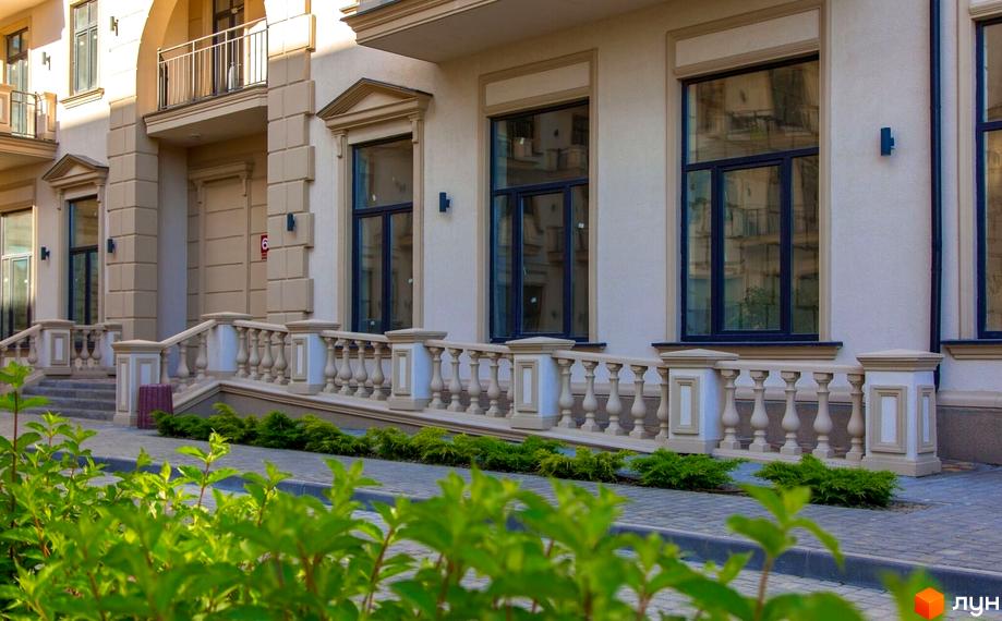 Фасад будинку Житлового кварталу Авторський з бежевими архітектурними елементами, великими вікнами та кам'яними балюстрадами. Перед будинком зелені кущі.