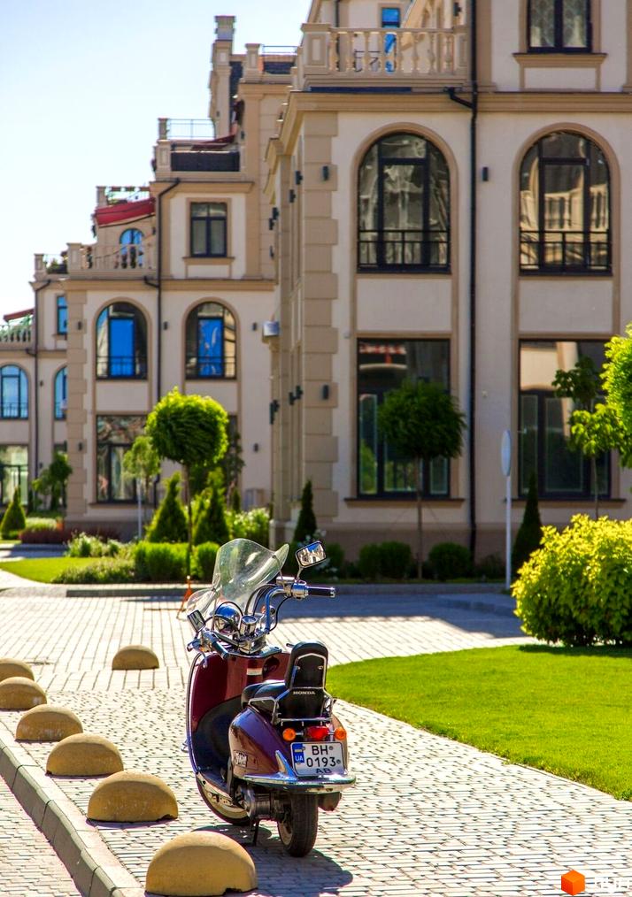 Фасади будинків Житлового кварталу Авторський з арковими вікнами та балконами. На передньому плані бруківка, зелені газони та доглянуті дерева.