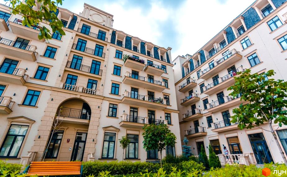 Житловий квартал Авторський: світлі житлові будівлі з декоративними елементами, мансардними дахами та балконами. Територія озеленена деревами та лавками.