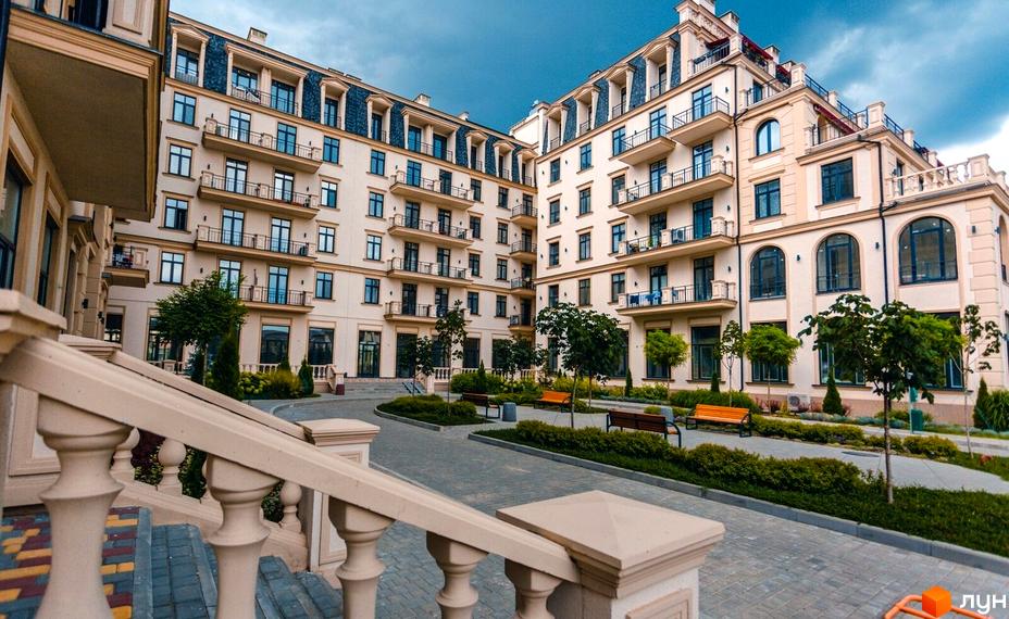 Світлі фасади житлового кварталу Авторський з балконами та великими вікнами. На передньому плані доглянута прибудинкова територія з деревами та лавками.