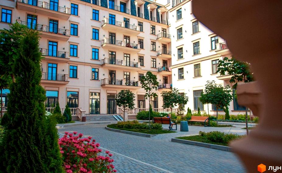 Житловий квартал Авторський: світлі будинки з балконами та синіми вікнами, оточені доглянутим двором з деревами та квітами.