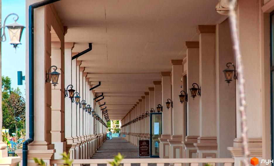 Довга колонада з рядами світлих колон та ліхтарів, що веде до зеленої зони з дитячим майданчиком у Житловому кварталі Авторський.