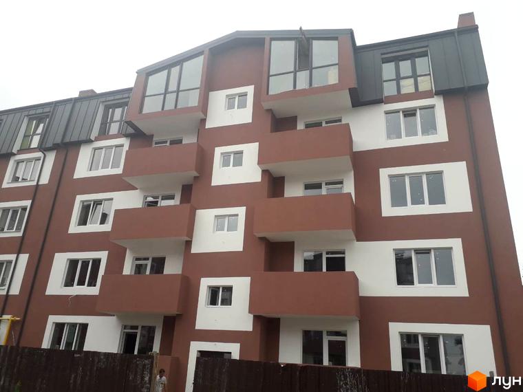 Зовнішній вигляд новобудови ЖК Гостомельські липки з коричневими та білими фасадами та балконами. Навколо будинку видно паркан.