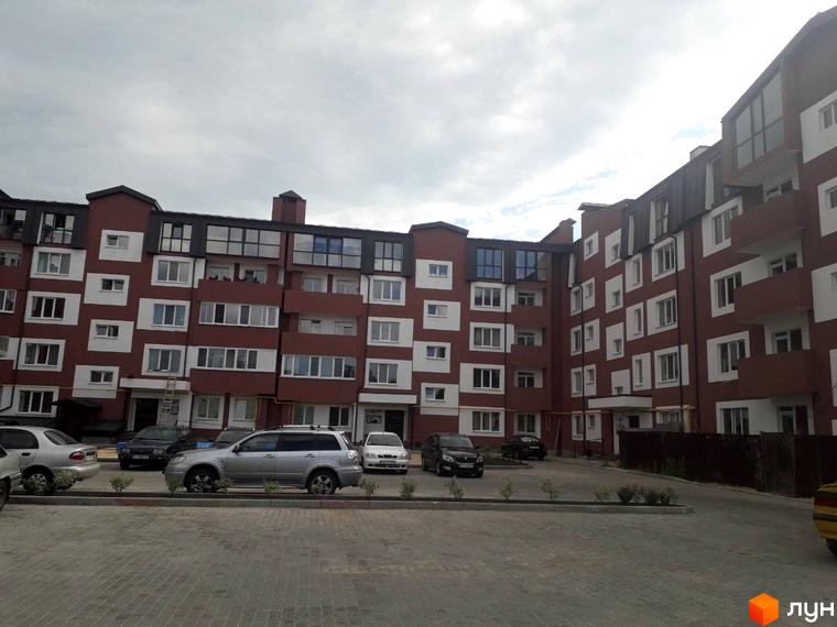 Зовнішній вигляд житлового комплексу Гостомельські липки з червоно-білими фасадами та парковкою з автомобілями.