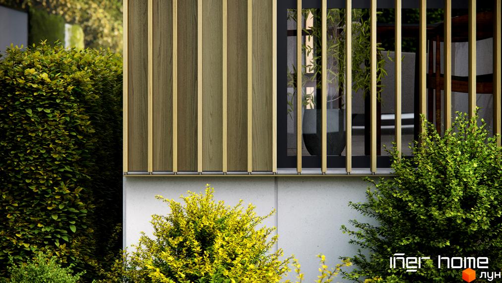 Фасад будинку з дерев'яними панелями та вікнами. На прибудинковій території зелені кущі та рослини.