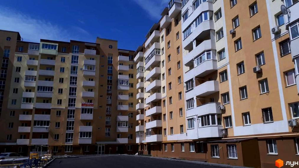 Багатоповерховий будинок ЖК Сонячний квартал з балконами та кондиціонерами на фасаді. Поруч розташована прибудинкова територія з асфальтованим покриттям.