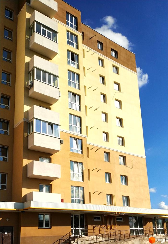 Висотна будівля ЖК Сонячний квартал з балконами та великими вікнами. На фото видно частину прибудинкової території та блакитне небо з хмарами.