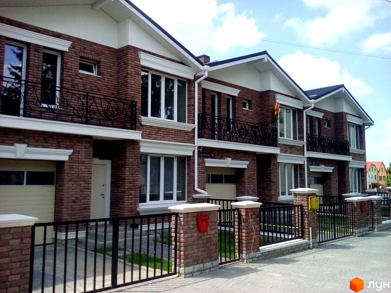 Ряд цегляних котеджів на вул. Євського, 18 з білими декоративними елементами та балконами. Територія огороджена металевим парканом з цегляними стовпами.