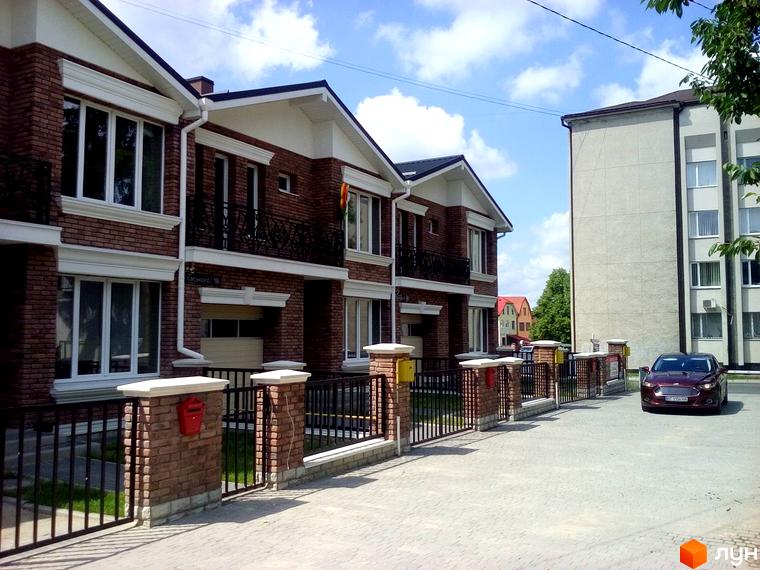 Новобудова на вул. Євського, 18: ряд цегляних таунхаусів з білими вікнами та балконами. Перед будинками бруківка та металевий паркан.