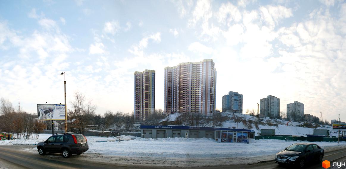 Вигляд ЖК Мозаїка з дороги. Високі будинки з великою кількістю вікон. На передньому плані дорога, автомийка та автомобілі.