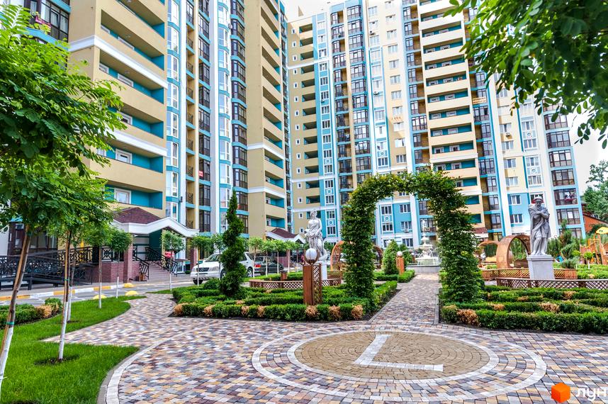 Житловий комплекс Версаль Парк. Фасад будинку в бежевих та блакитних тонах, зелена прибудинкова територія з арками та скульптурами.