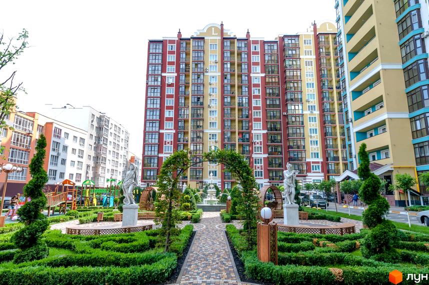 Житловий комплекс Версаль Парк: фасади будинків у червоних та жовтих тонах, доглянута прибудинкова територія зі скульптурами та зеленими насадженнями.