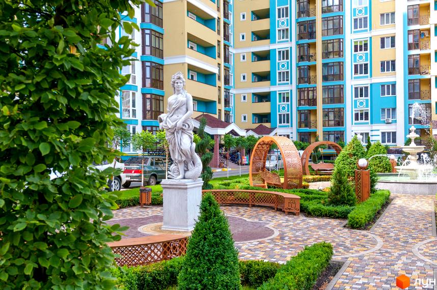 Житловий комплекс Версаль Парк. Фасади будівель у жовто-блакитних тонах, з елементами декору. Прибудинкова територія з парковою зоною, скульптурами та фонтаном.