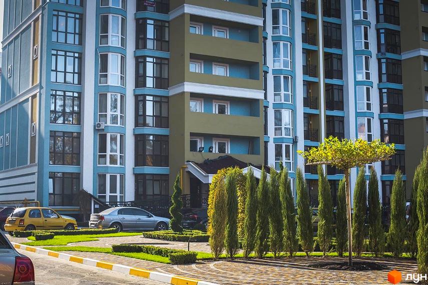 Новобудова ЖК Версаль Парк з блакитними та оливковими фасадами, великою кількістю вікон та доглянутою прибудинковою територією з зеленими насадженнями.