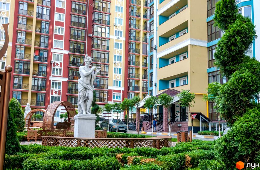 Житловий комплекс Версаль Парк: фасади будівель у червоних та жовтих тонах, з блакитними акцентами. Прибудинкова територія з парковою зоною, скульптурою та зеленими насадженнями.
