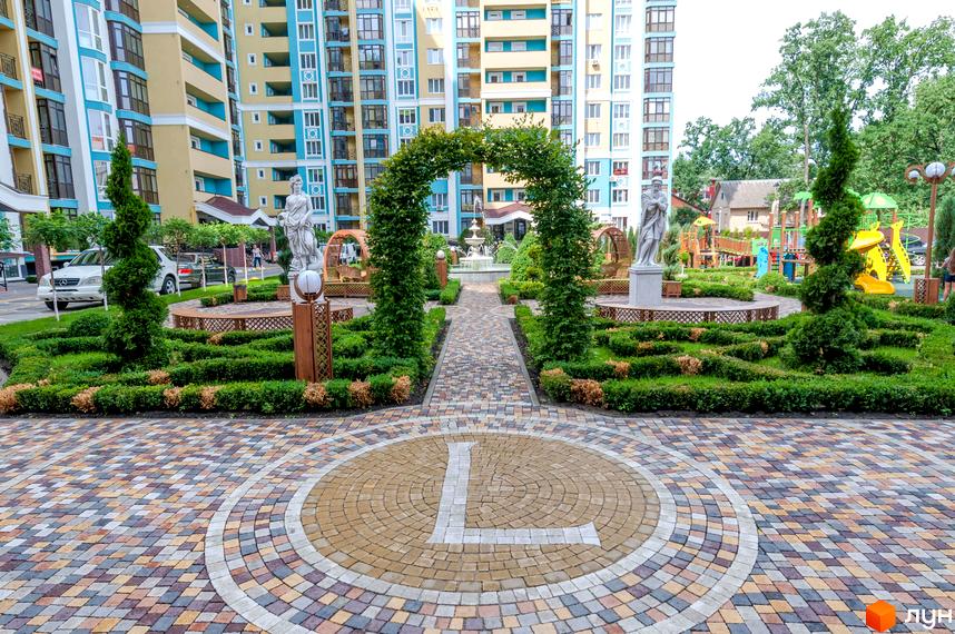 Житловий комплекс Версаль Парк: фасади багатоповерхових будинків та доглянута прибудинкова територія з аркою та скульптурами.