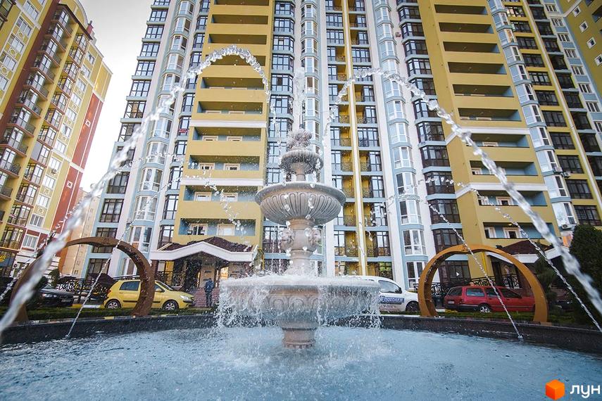 Житловий комплекс Версаль Парк з фонтаном та автомобілями на прибудинковій території. Сучасна архітектура новобудови з жовтими та блакитними фасадами.