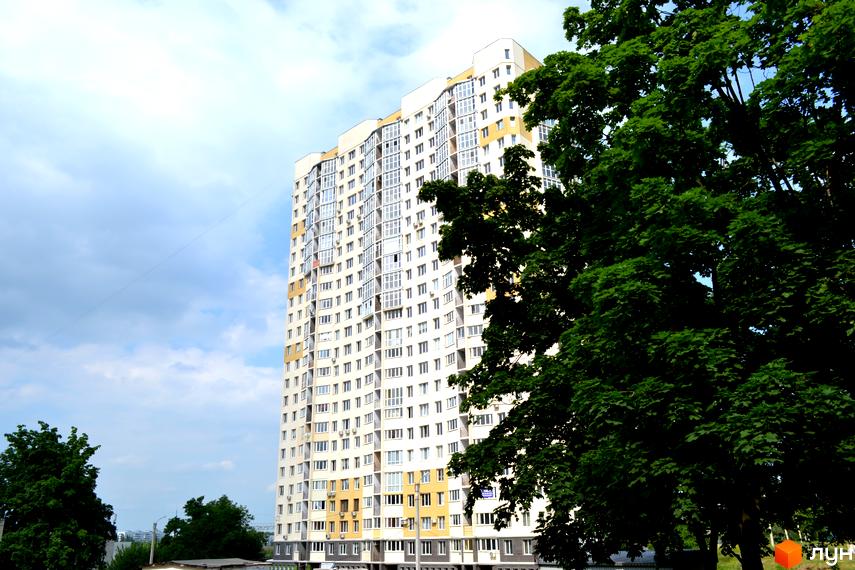 Багатоповерховий житловий будинок Житлового комплексу Ювілейний світлого кольору з хвилястим фасадом та численними вікнами. Частина будівлі оточена зеленими деревами.