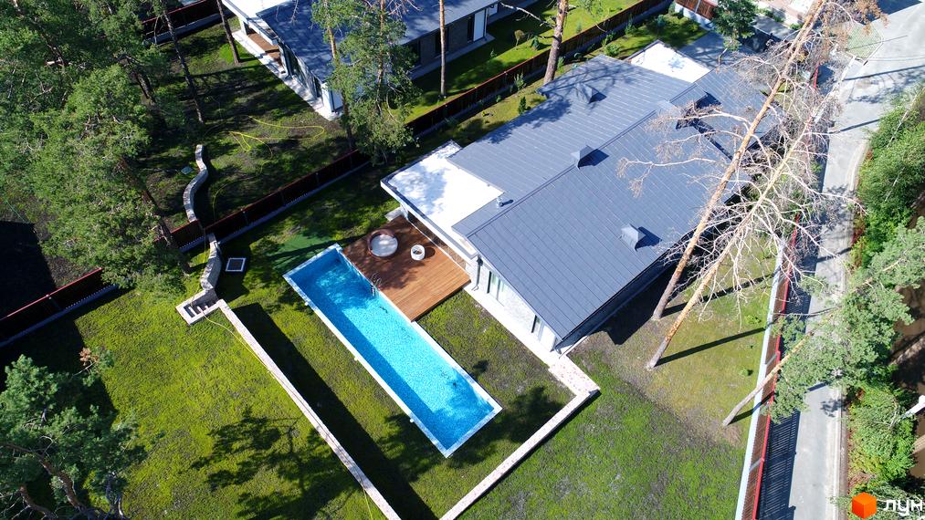 Будинок Котеджного містечка Хвойний квартал з сірим металевим дахом та світлими фасадами, оточений зеленим газоном, басейном і хвойними деревами.