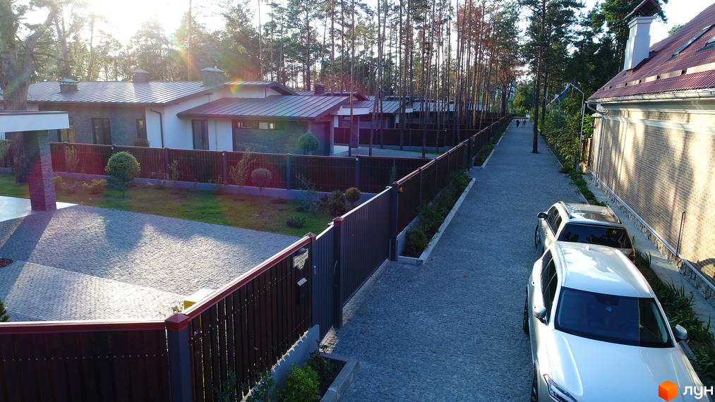 Будинки Котеджного містечка Хвойний квартал з темними дахами та світлими стінами, розташовані серед хвойних дерев біля брукованої доріжки.